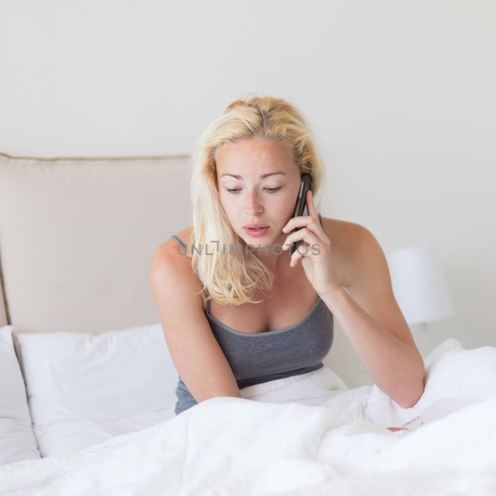 Portrait of  young lady with mobile phone in bed at home. Tired sleepy woman receiving emergency call in bed early in the morning.