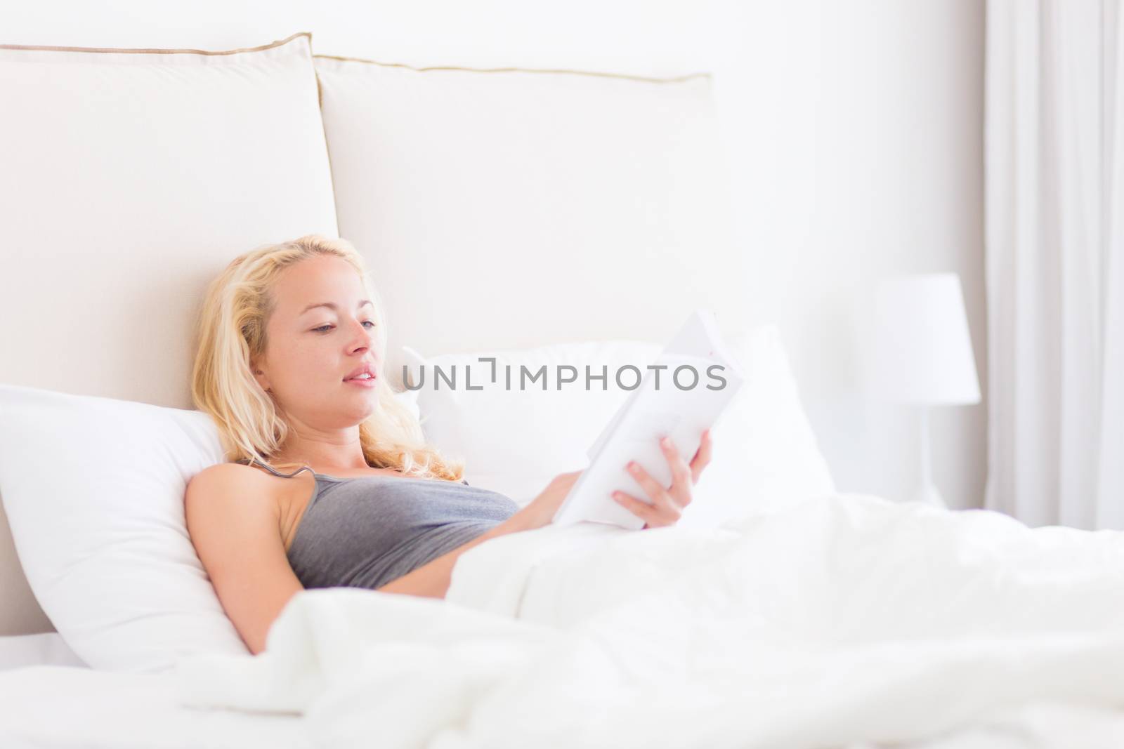 Young Caucasian woman reading book while lying in bed.