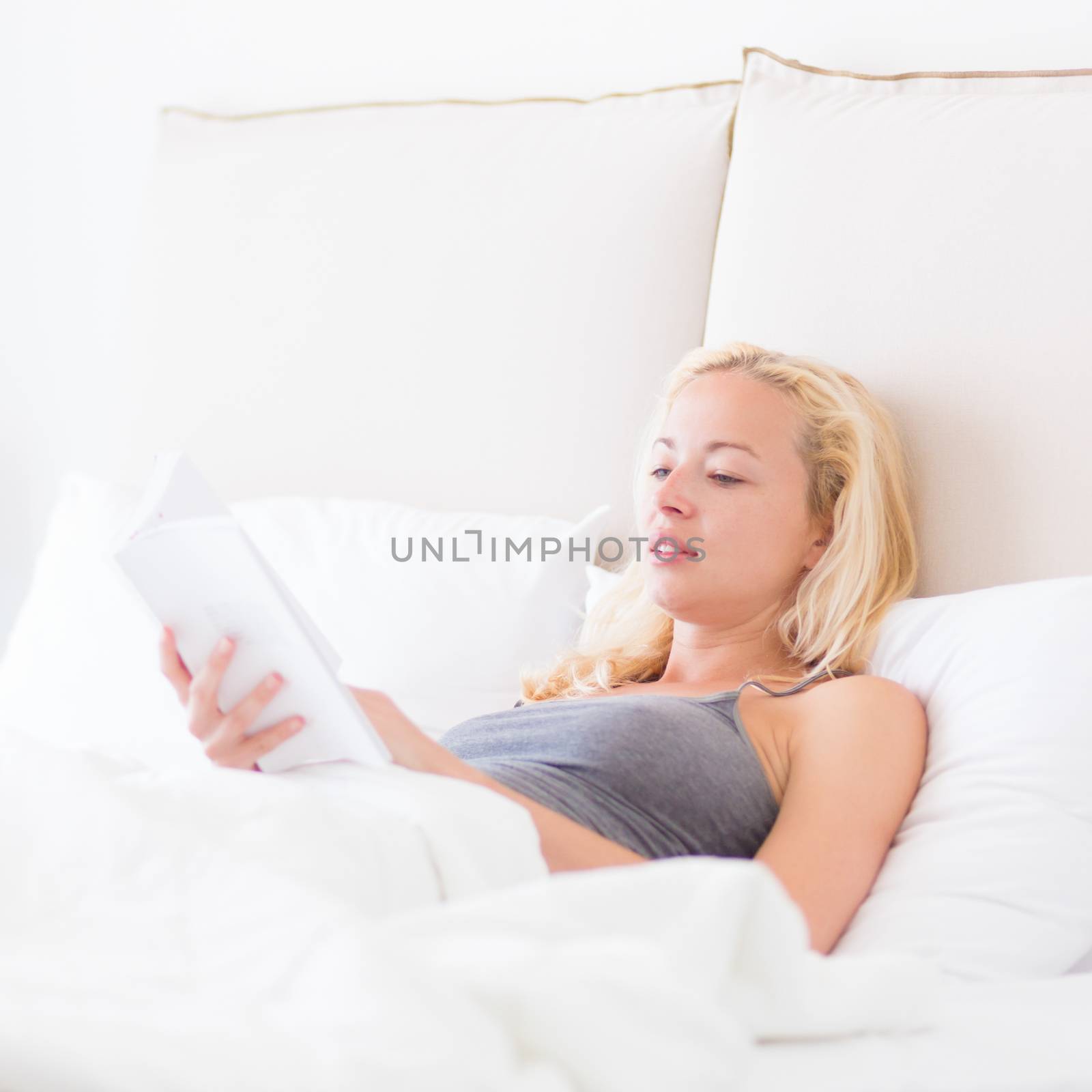 Young Caucasian woman reading book while lying in bed.