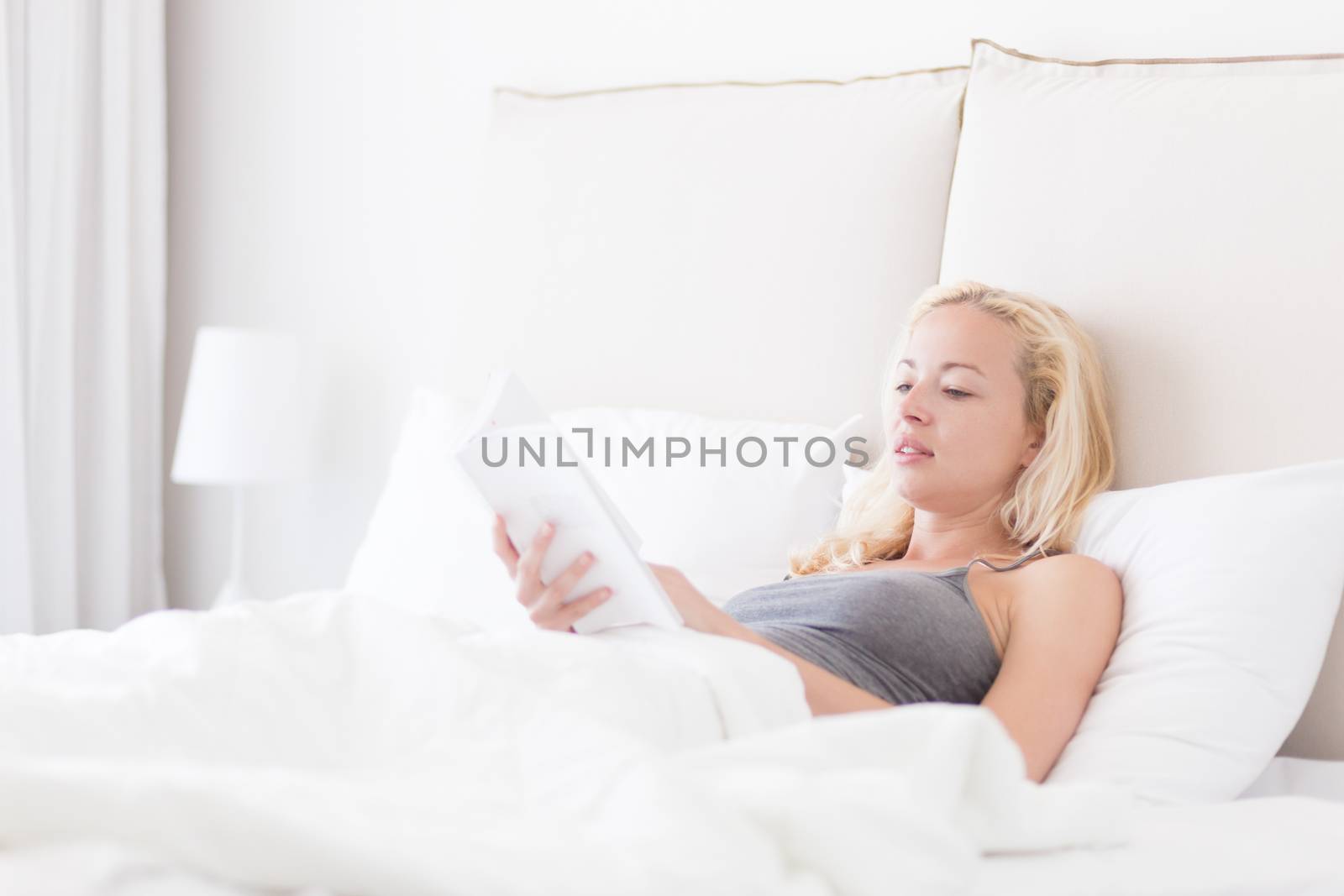 Young Caucasian woman reading book while lying in bed.