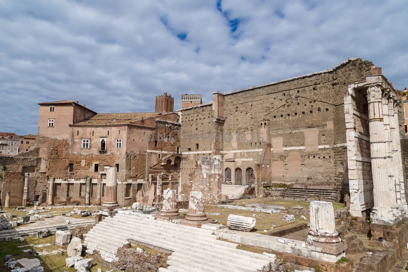 View of an ancient Roman Forum with columns and ruins around in Rome, with tourists around, on cloudy sky background.