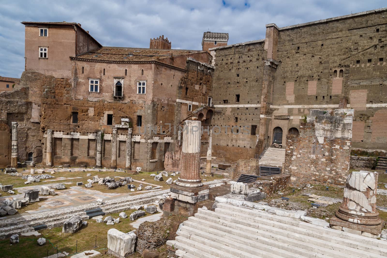 View of an ancient Roman Forum with columns and ruins around in Rome, with tourists around, on cloudy sky background.