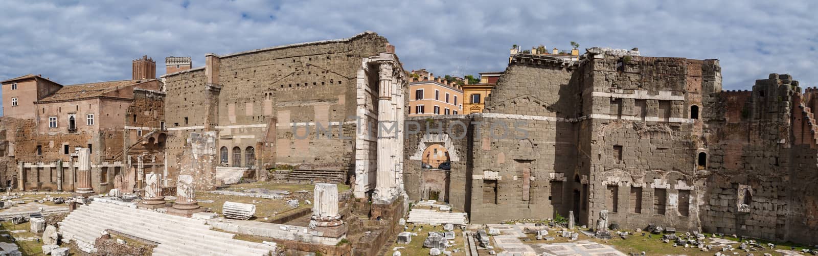 View of an ancient Roman Forum with columns and ruins around in Rome, with tourists around, on cloudy sky background.