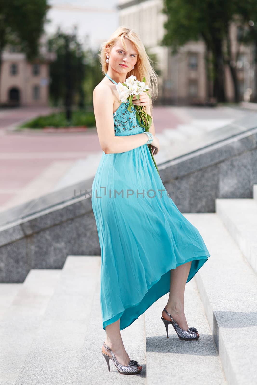 Blond Girl on stairs with flower on hand in fashion dress