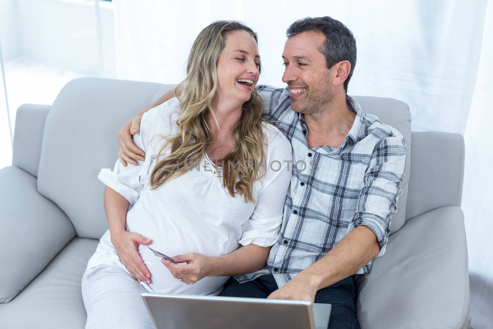 Expecting couple sitting on sofa and using laptop