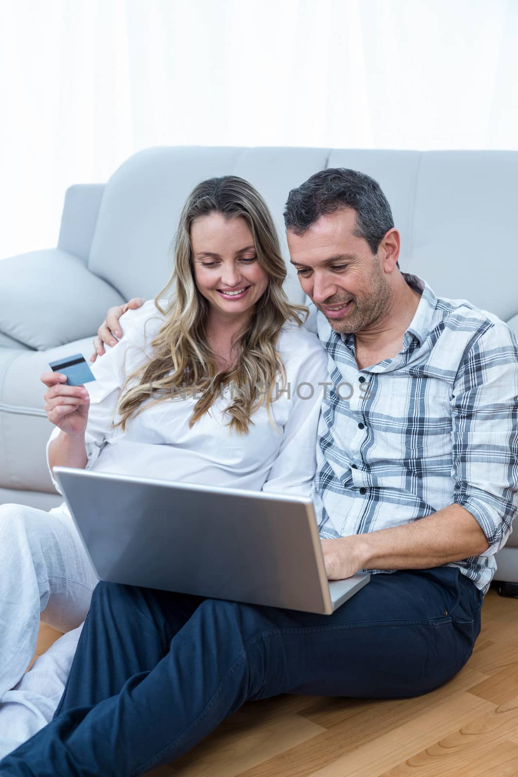 Expecting couple sitting on sofa and using laptop