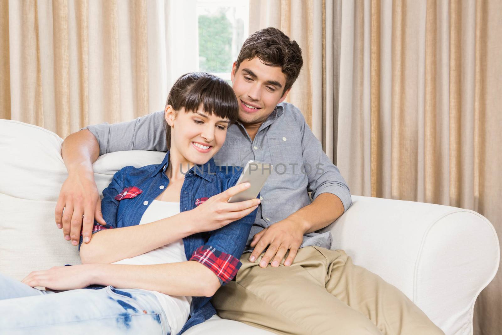 Romantic couple at home relaxing on the sofa using mobile phone