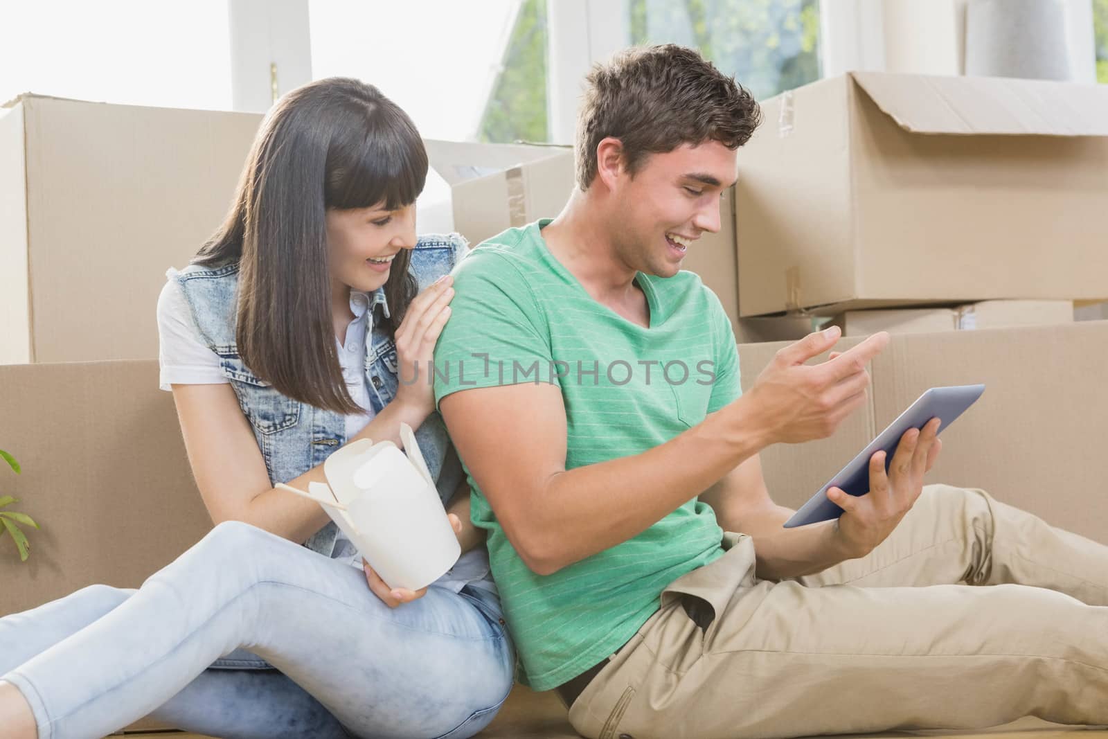 Young couple eating noodle and using digital tablet in their new house