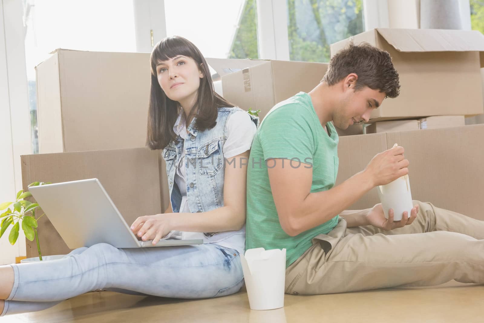 Young couple eating noodle and using laptop in their new house