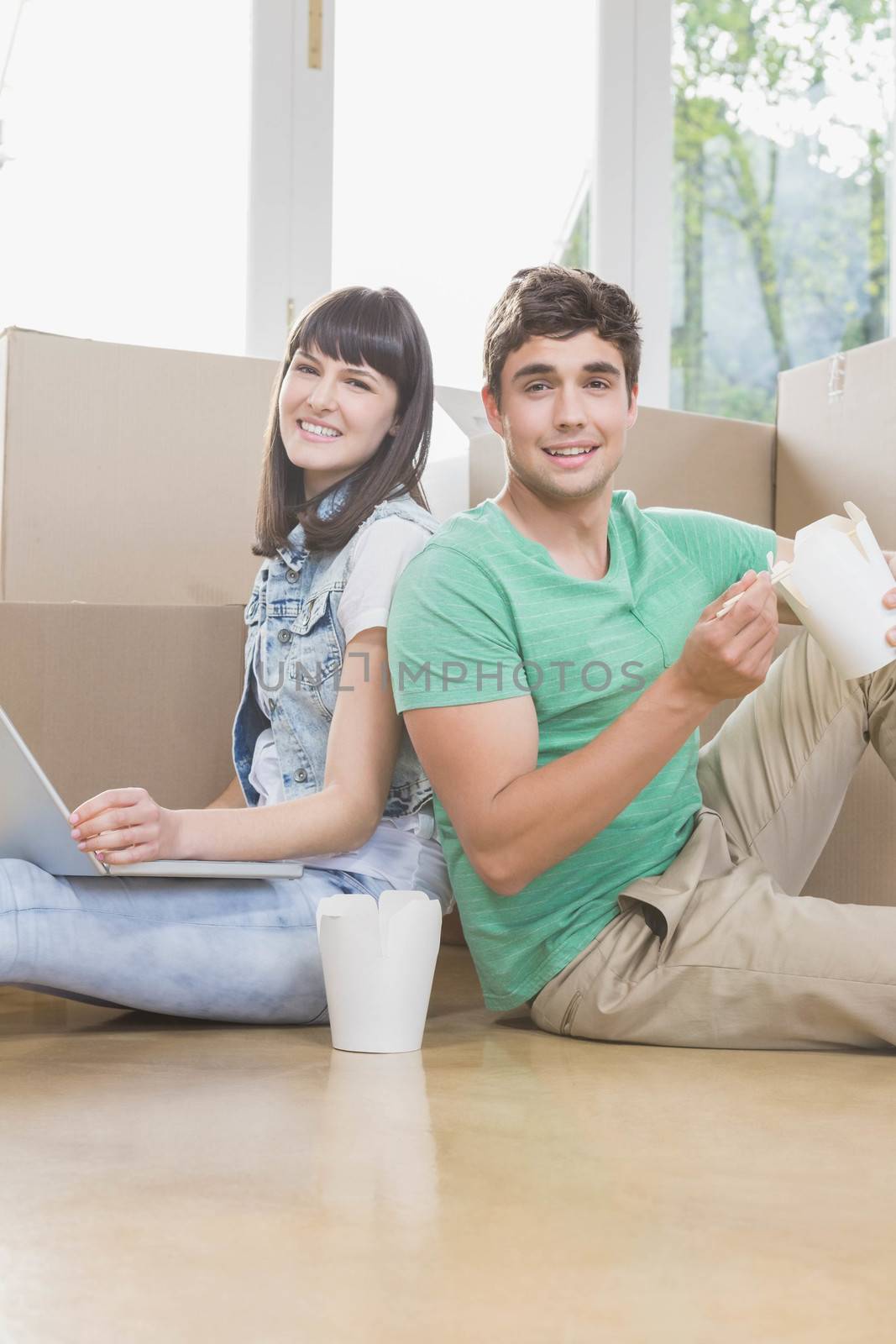 Young couple eating noodle and using laptop in their new house