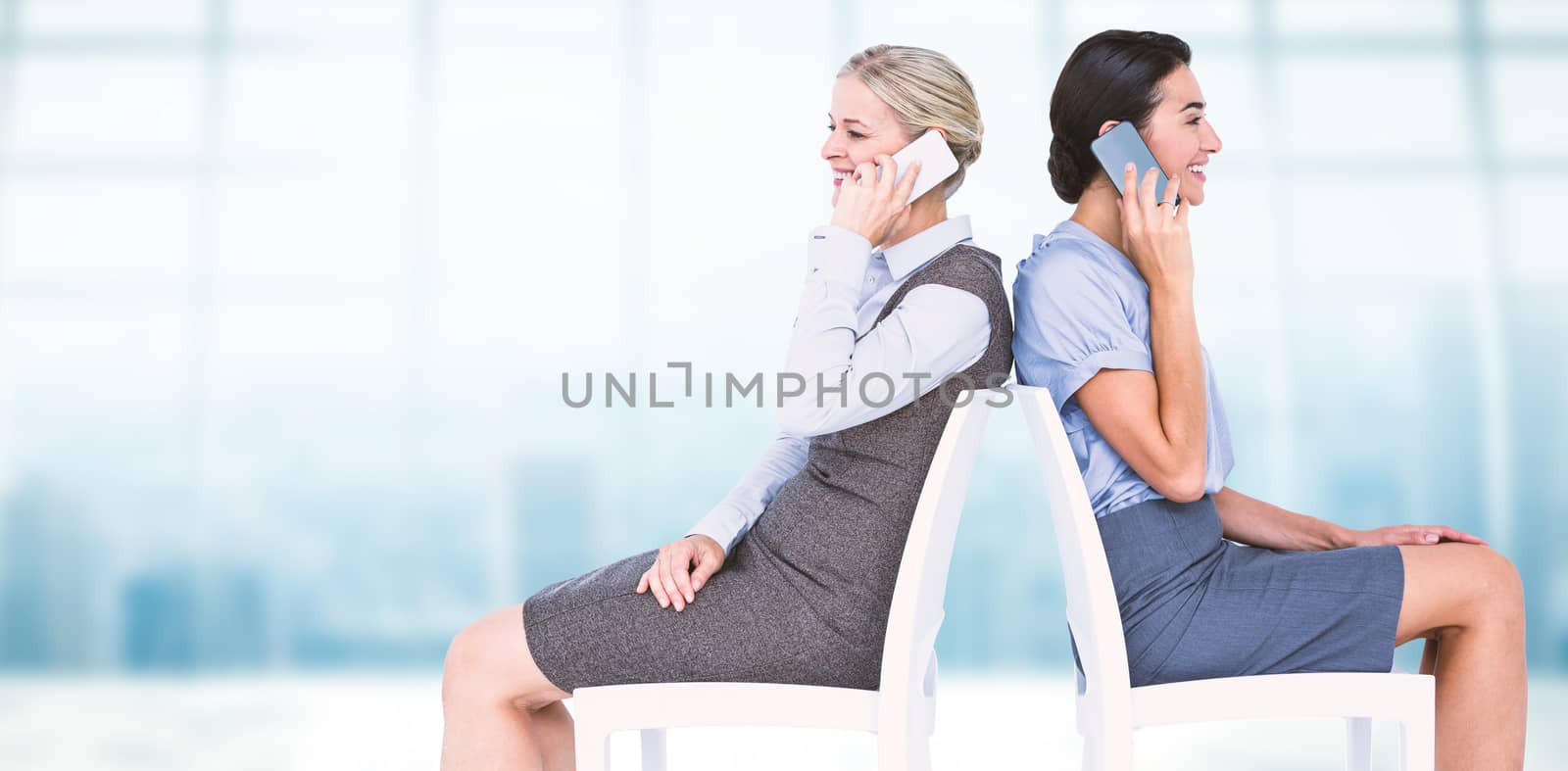 Businesswomen using smartphones while sitting on chair against modern room overlooking city