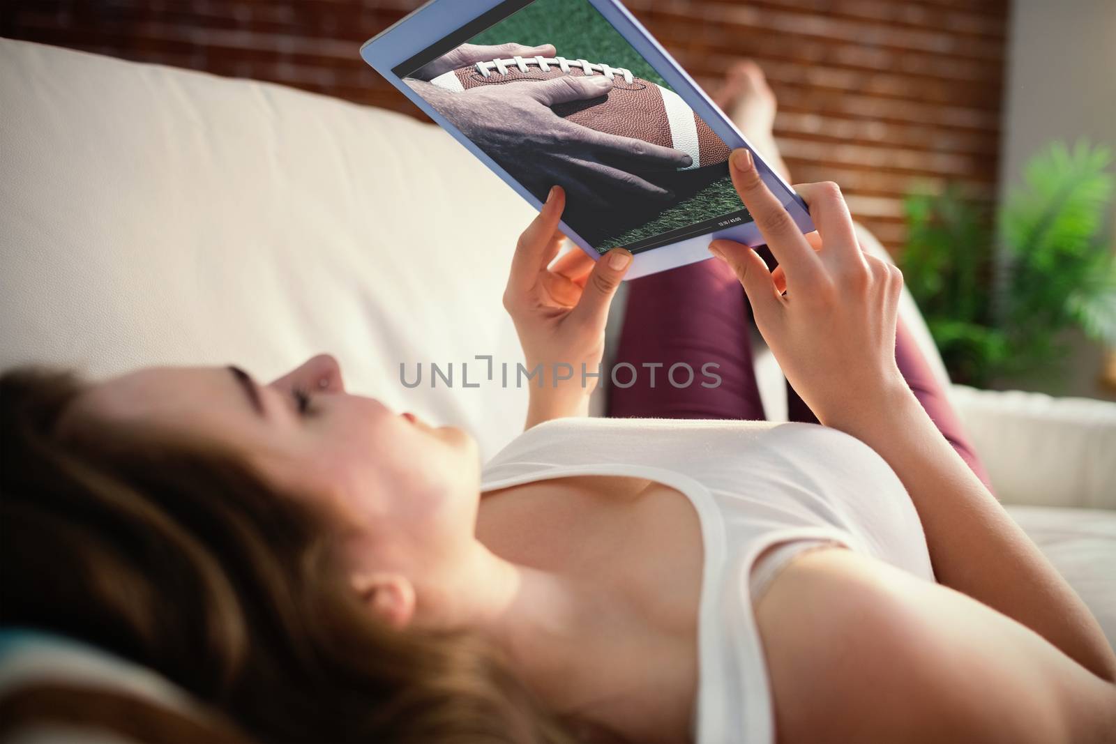 Close up view of american football player preparing for a drop kick against pretty woman lying on the couch while using tablet