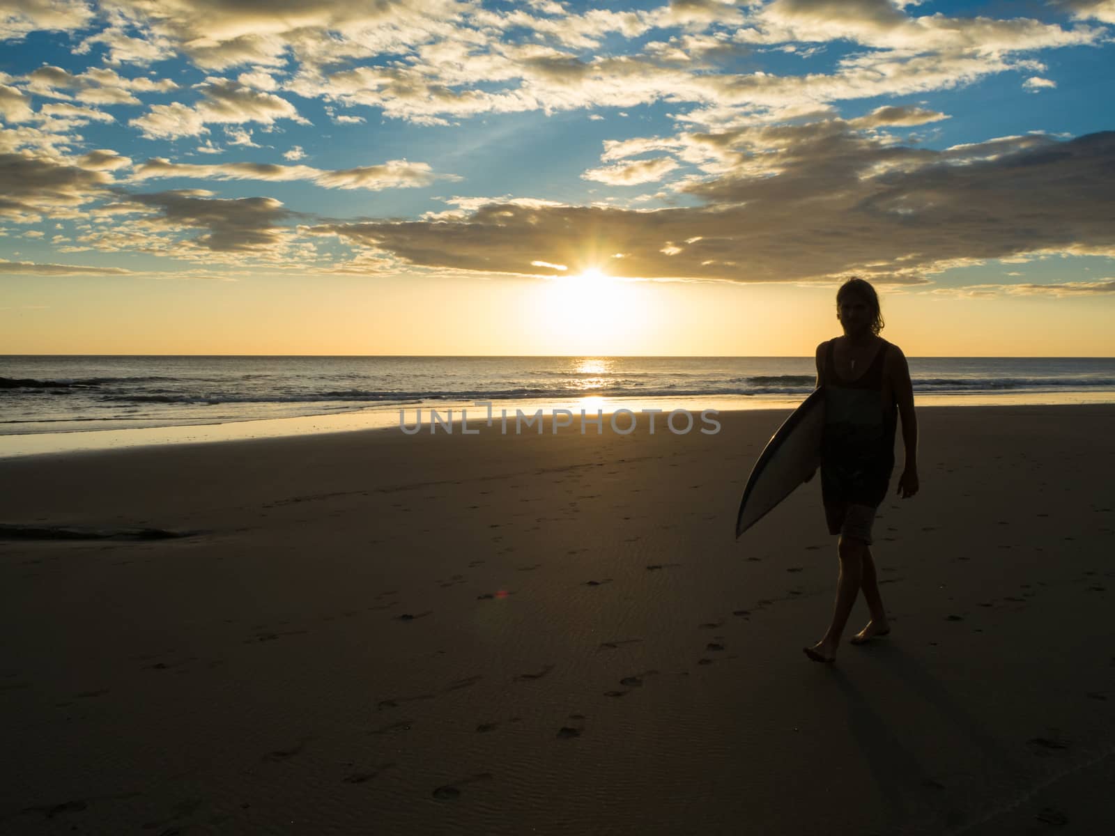 Surfer walks on the beach at the sunrise or sunset
