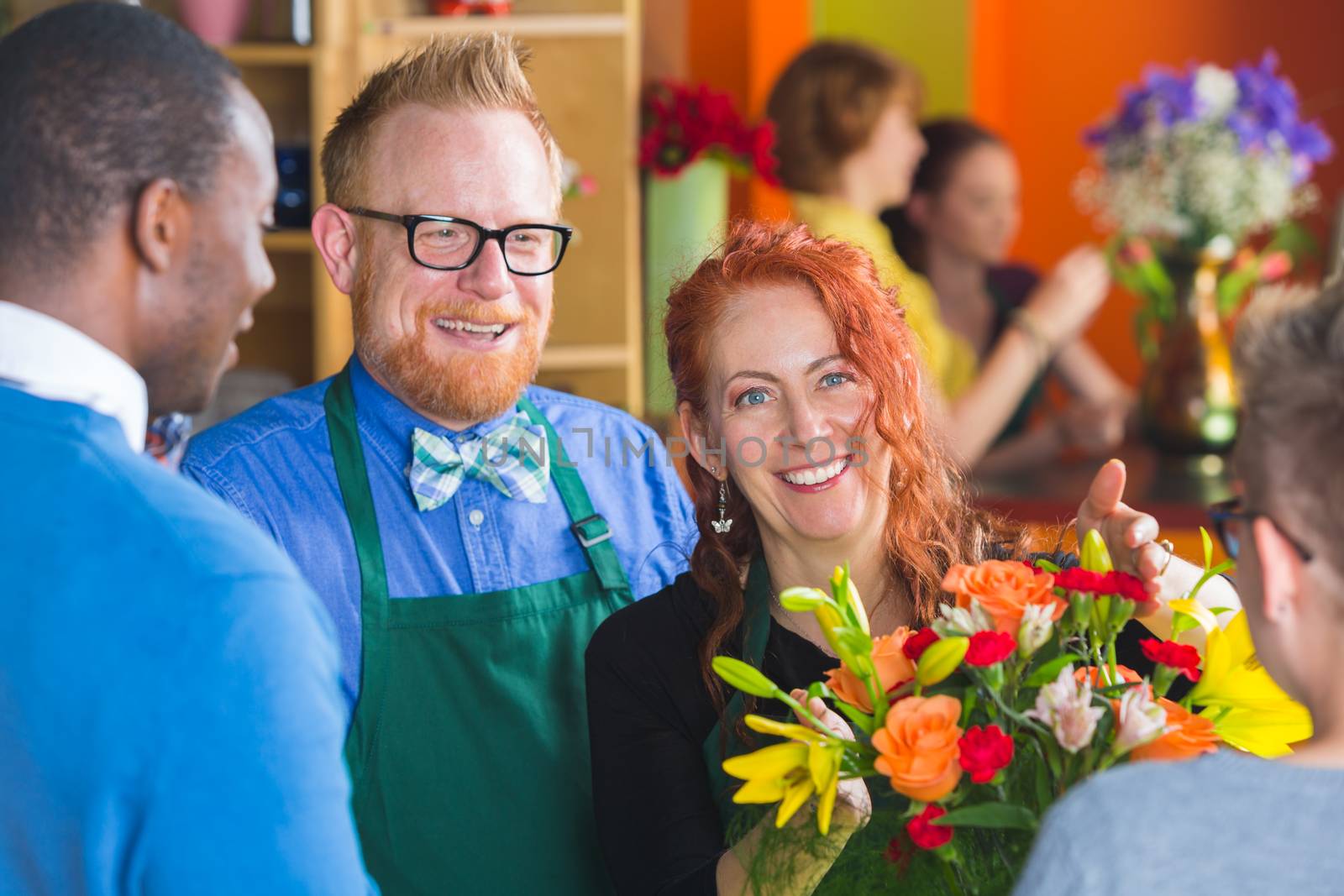 Female owner of busy flower shop handing floral arrangement to customers