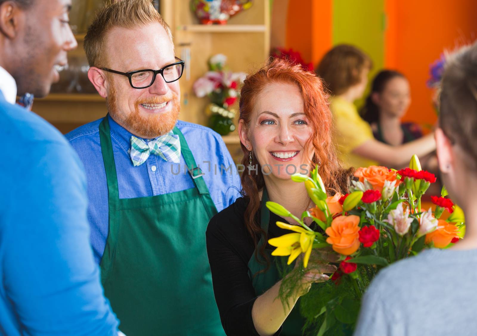 Happy bearded man with eyeglasses and apron working with woman in busy flower shop