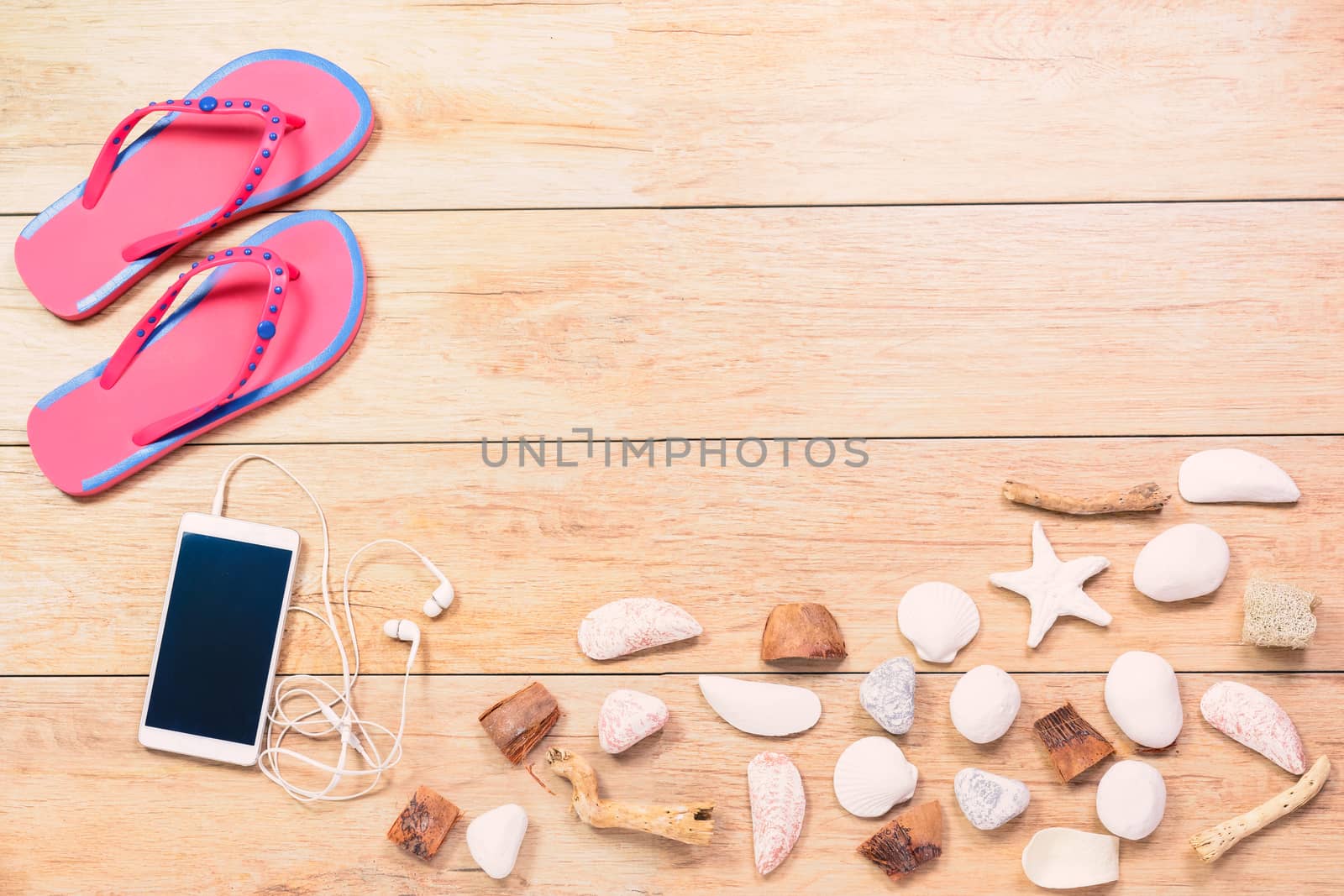 Pictured beach slippers, phone with earphones and shells on wooden boards background.