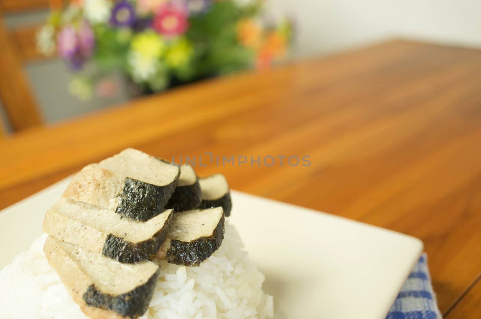 Vegetarian fried salted fish slice and white rice with blue fabric on wood table and blur flower as background.