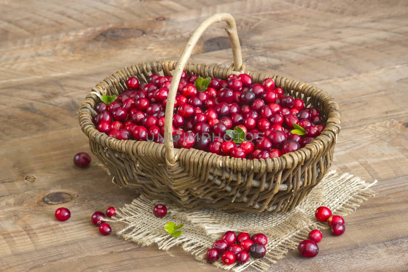 Cranberries in a basket on wooden background.