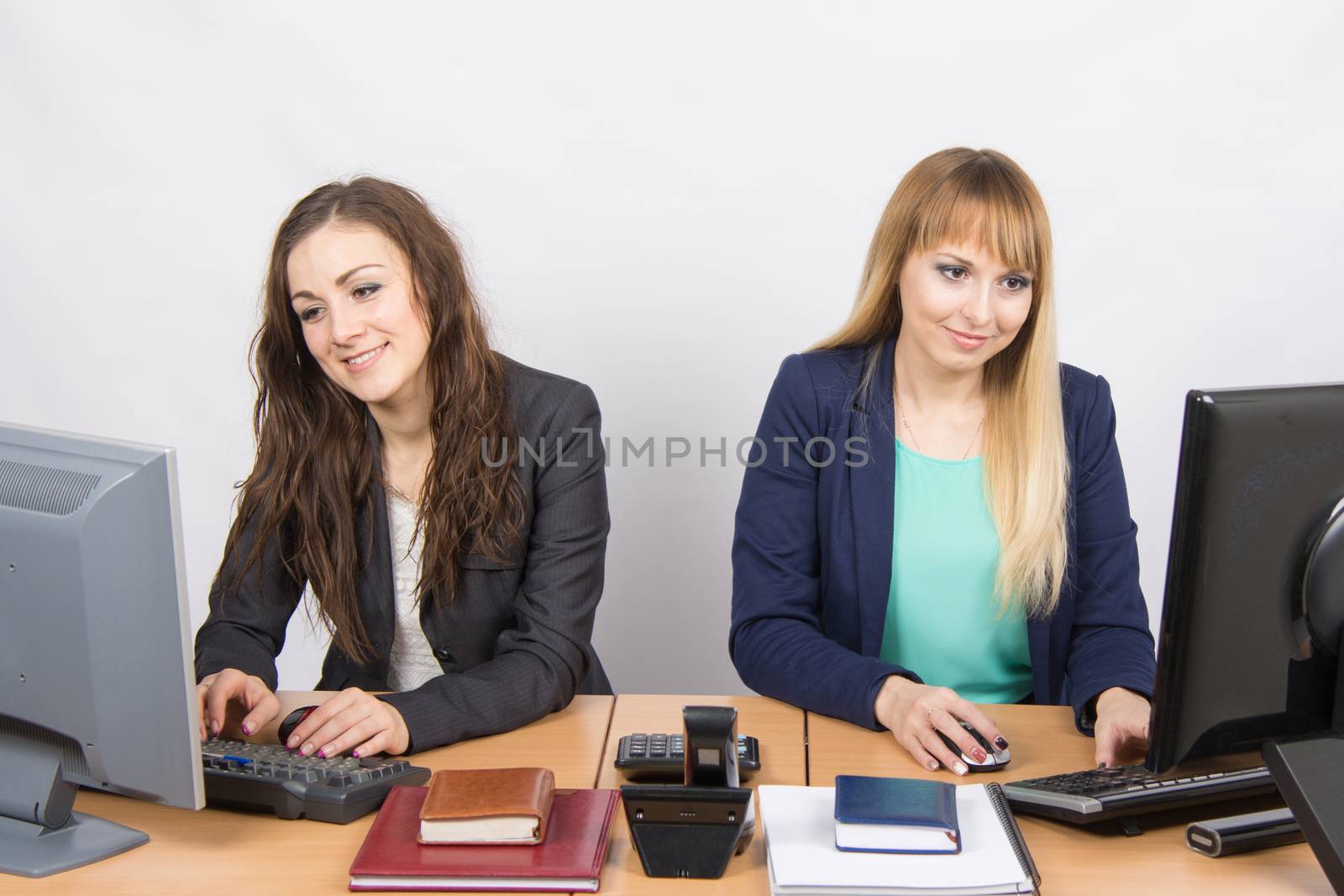Two young pretty business woman sitting at a office table is divided into two jobs