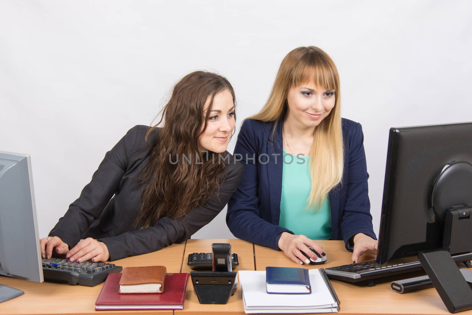 Two young pretty business woman sitting at a office table is divided into two jobs