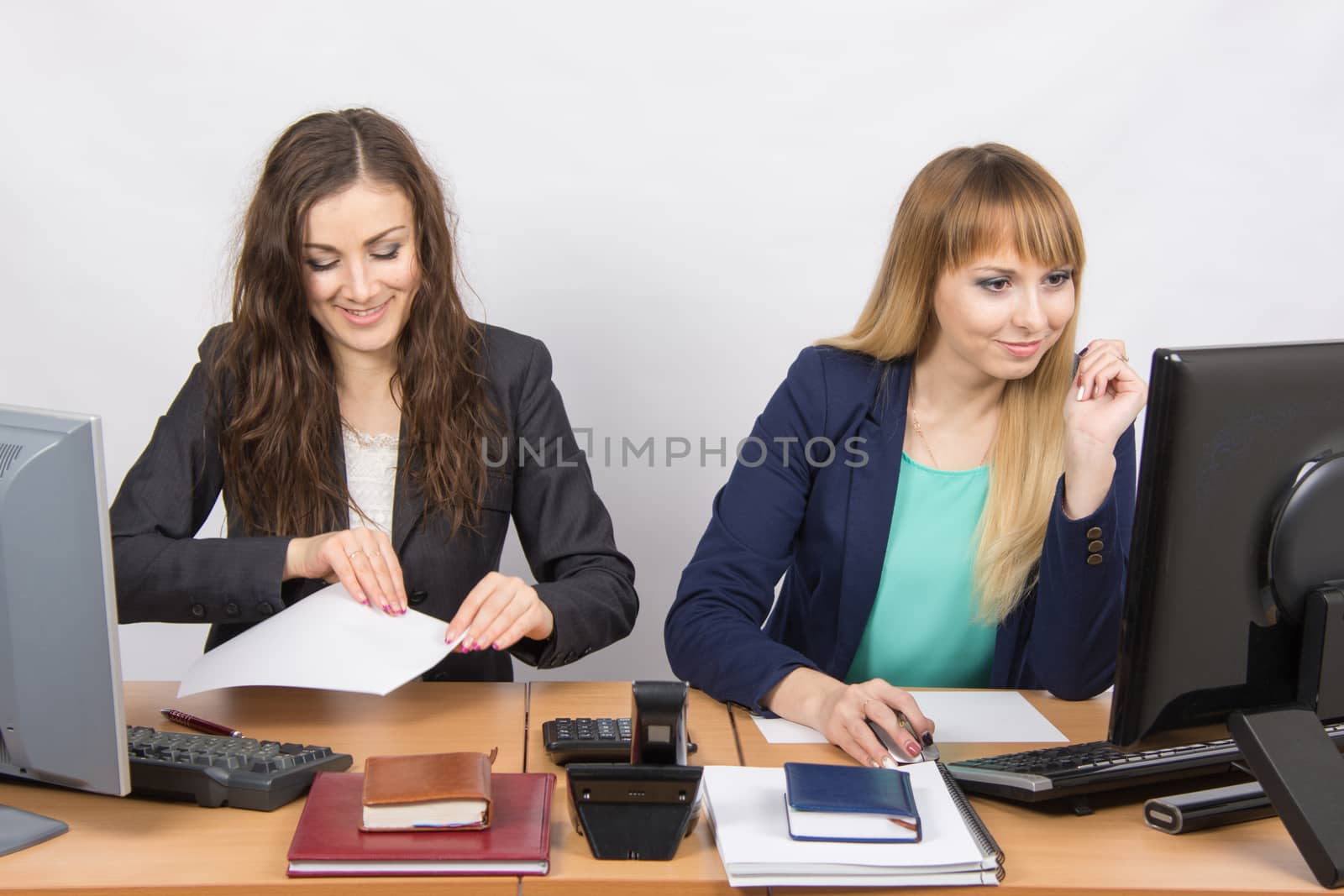 Two young pretty business woman sitting at a office table is divided into two jobs