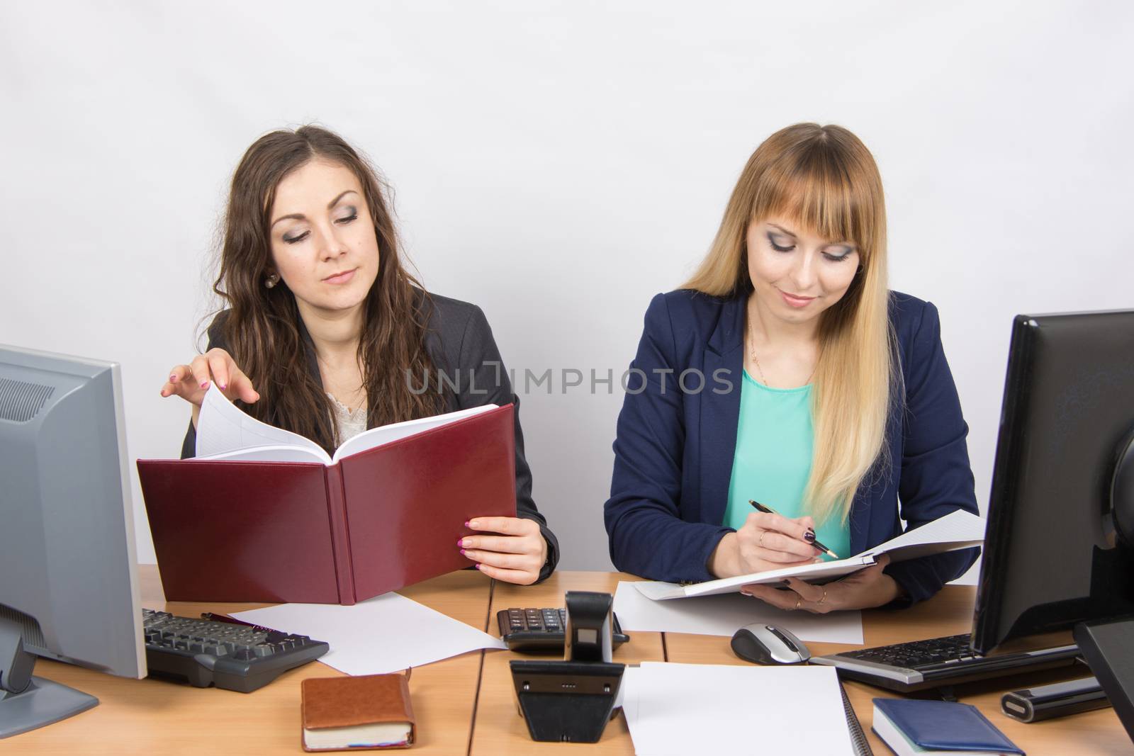 Two young pretty business woman sitting at a office table is divided into two jobs