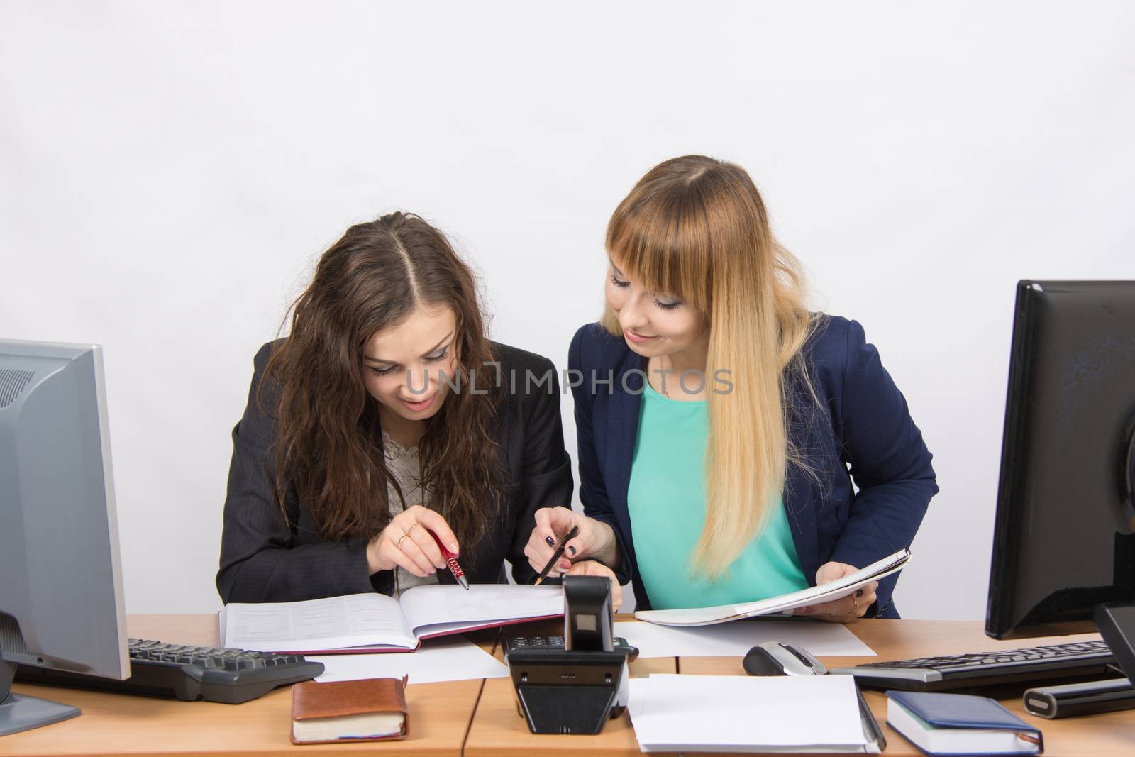 Two young pretty business woman sitting at a office table is divided into two jobs