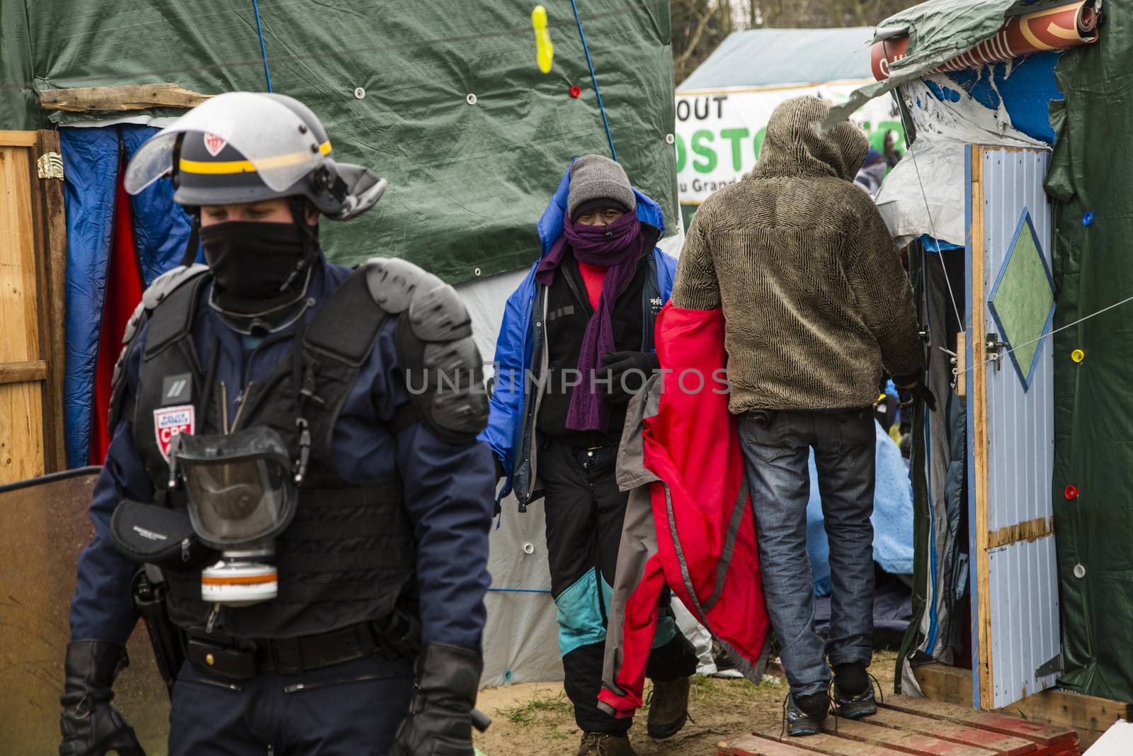 FRANCE, Calais: A riot police officer stands next to migrants as agents dismantle shacks and shelters in the Jungle migrant camp, in the French northern port city of Calais, on March 1, 2016. Workers were due to start a second day of destruction in the southern half of the camp, where thousands of migrants and refugees have been living while they try to reach Britain.