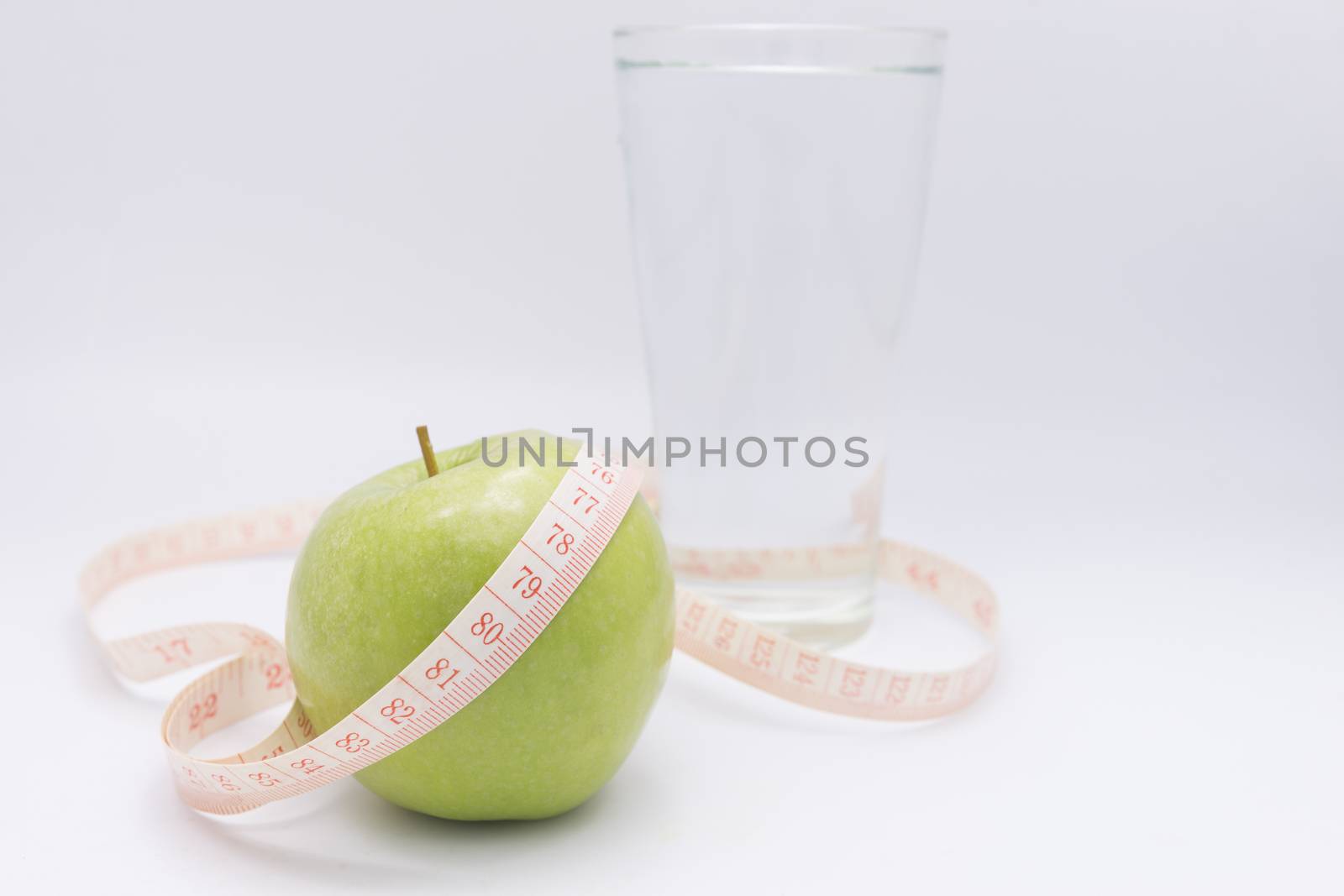 A green apple with a measuring tape wrapped around it for the concept of dieting.