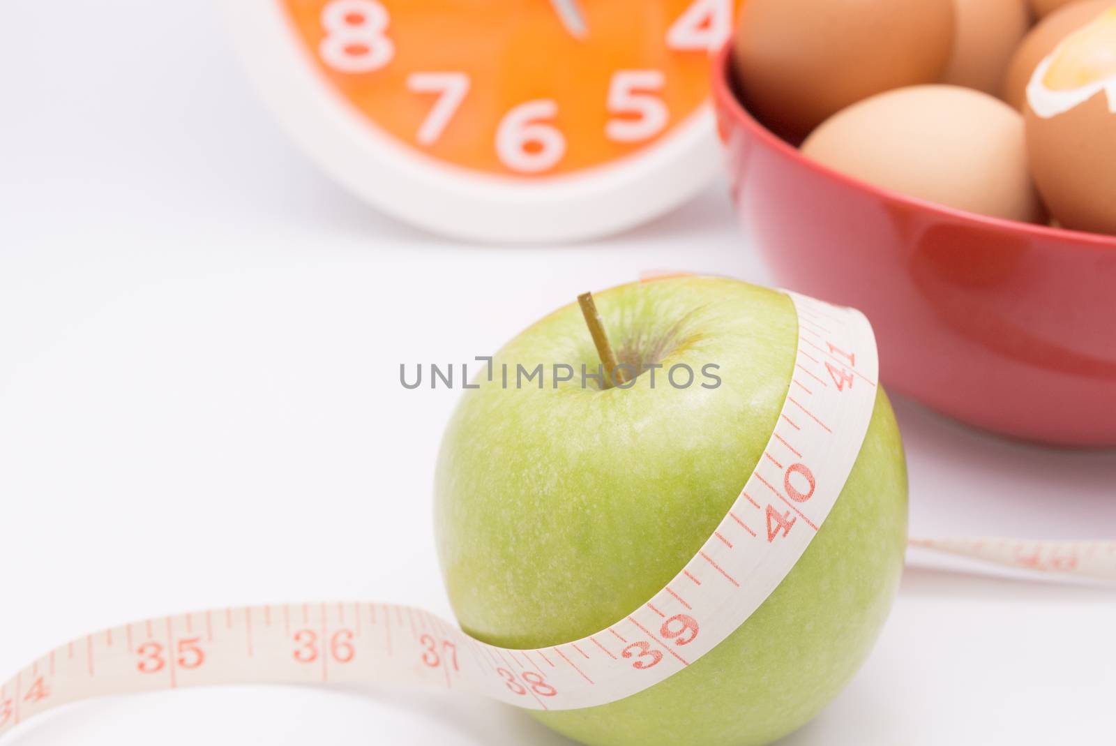 A green apple with a measuring tape wrapped around it and orange clock  for the concept in dieting and time to start