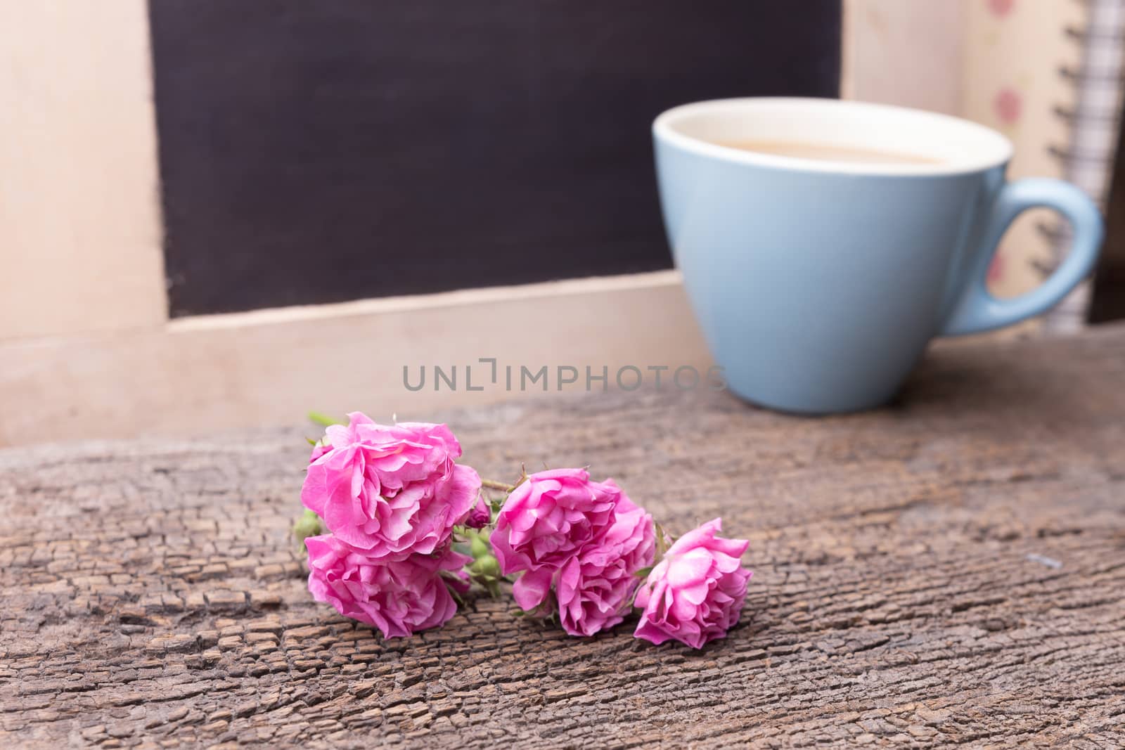 Pink rose and mug with coffee on a wooden table.  by frank600