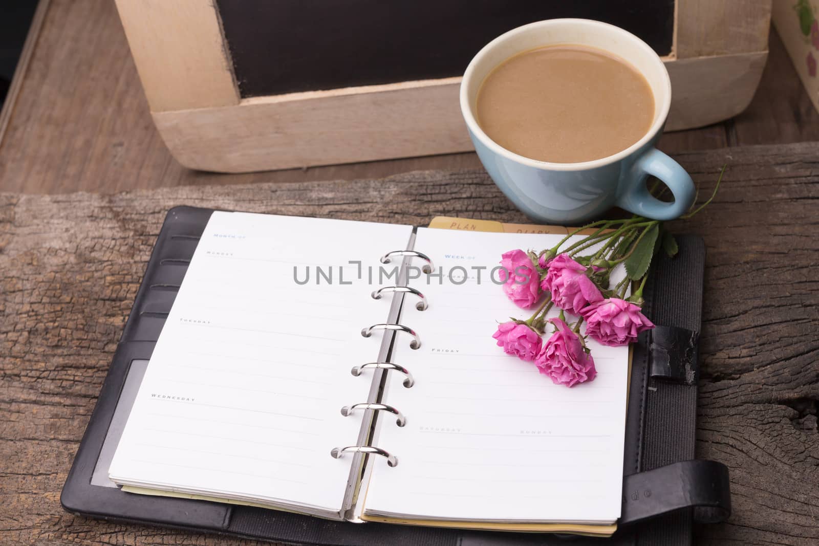 Weekend concept. Pink rose, mug with coffee, diary for note on a wooden table. Selective focus, copy space background