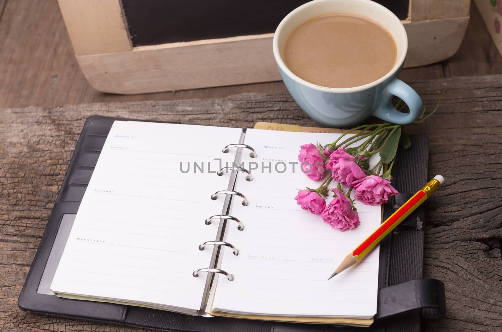 Weekend concept. Pink rose, mug with coffee, diary and pencil on a wooden table. Selective focus, copy space background