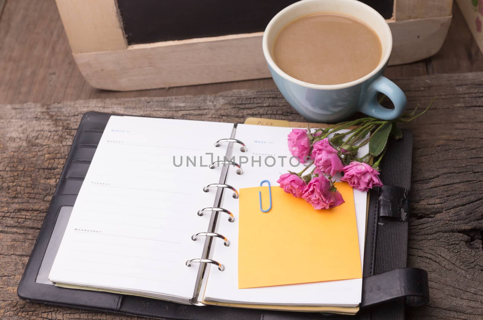 Weekend concept. Pink rose, mug with coffee, diary and stcky notel on a wooden table. Selective focus, copy space background