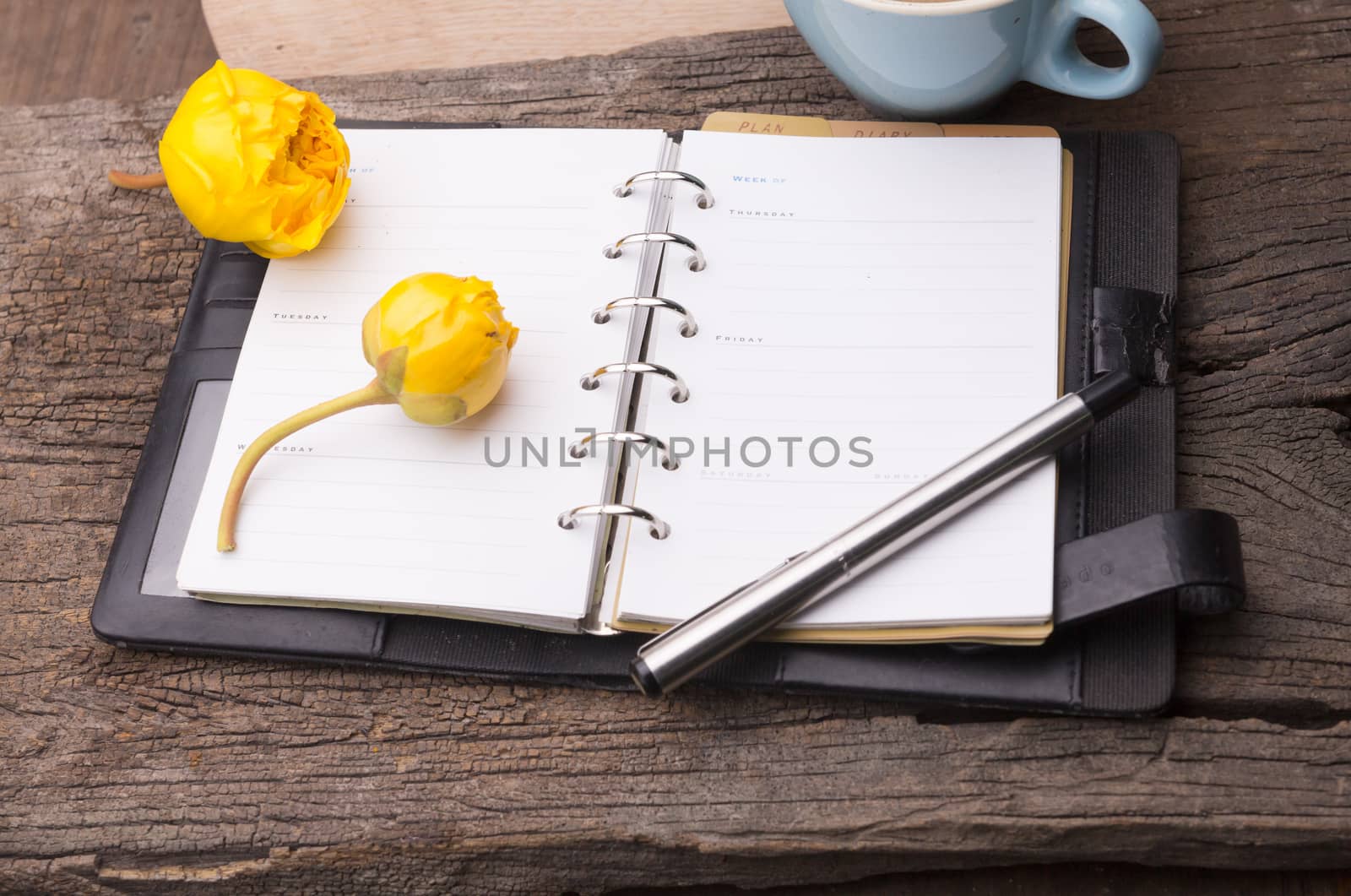 Weekend concept. yellow flowers, mug with coffee, diary and pencil on a wooden table. Selective focus, copy space background