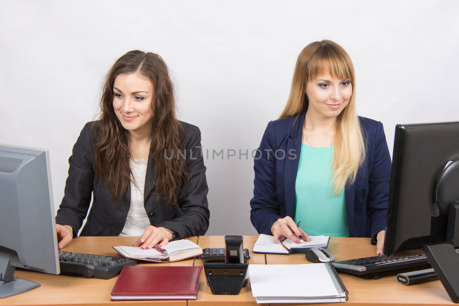 Two young pretty business woman sitting at a office table is divided into two jobs
