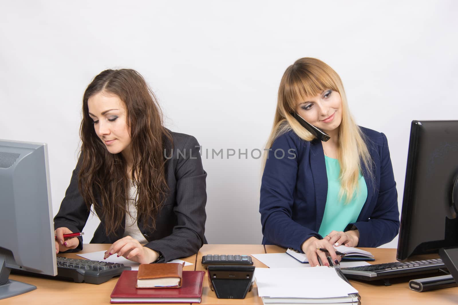 Two young pretty business woman sitting at a office table is divided into two jobs
