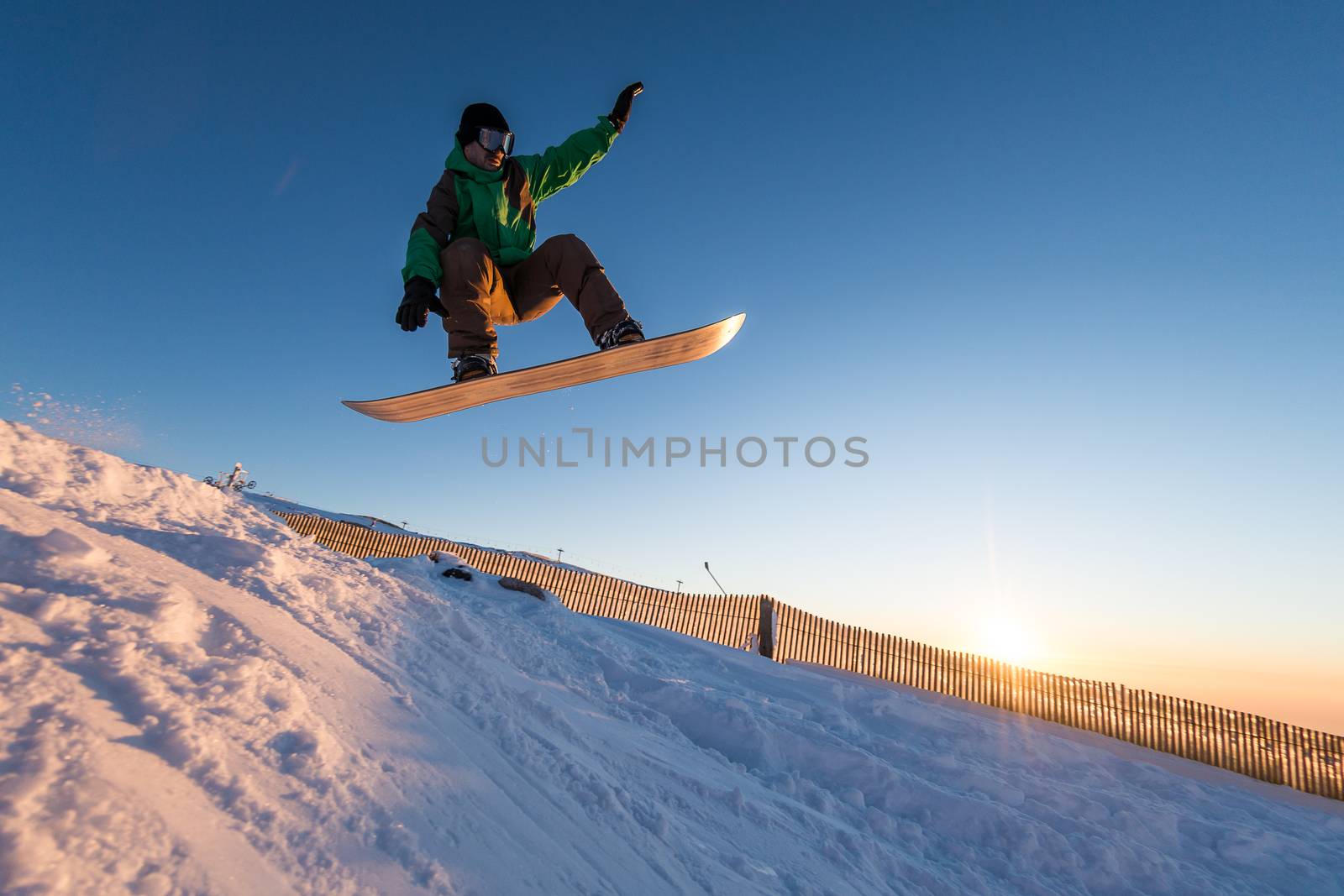 Snowboarder at jump in mountains at sunset sky.