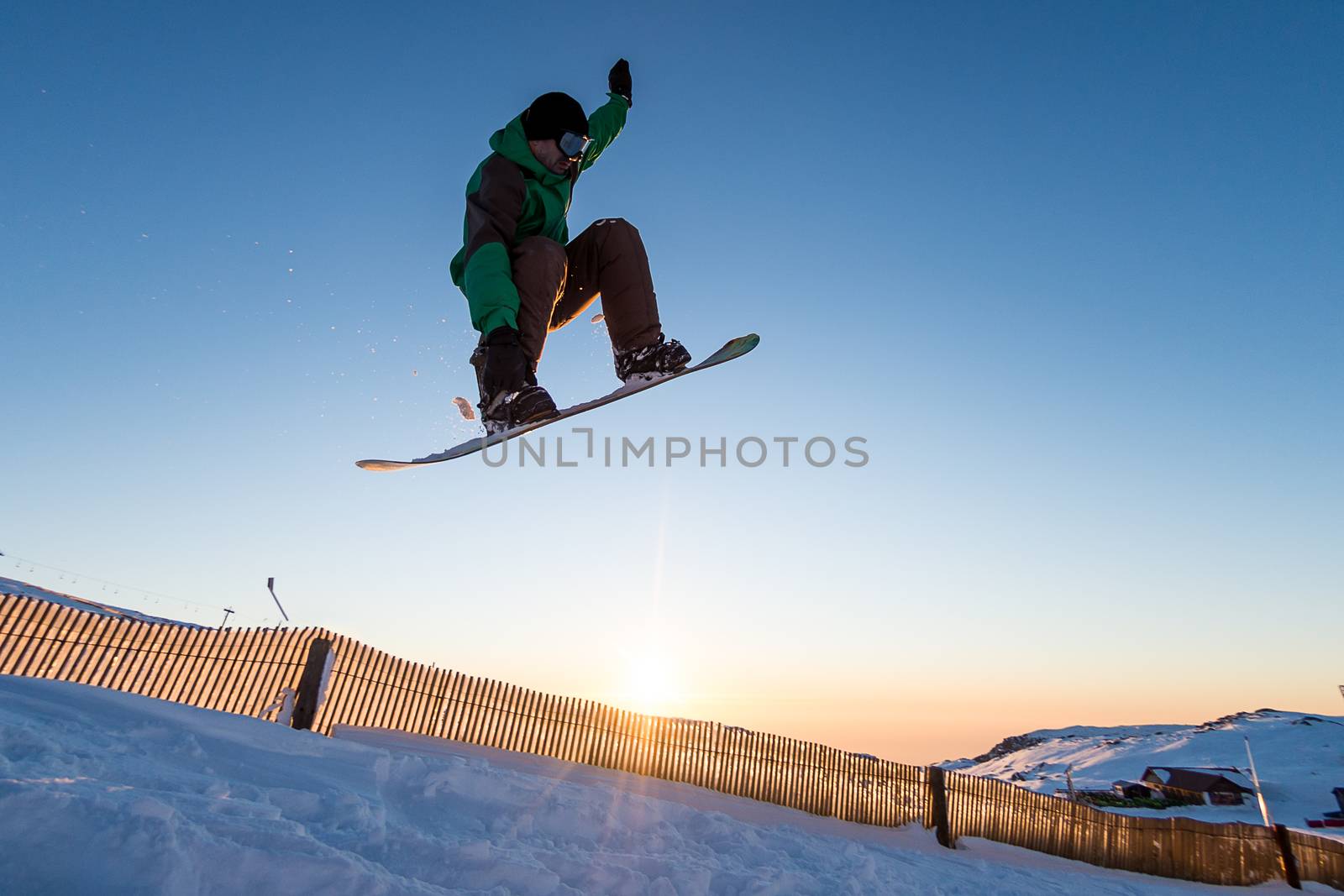 Snowboarder at jump in mountains at sunset sky.