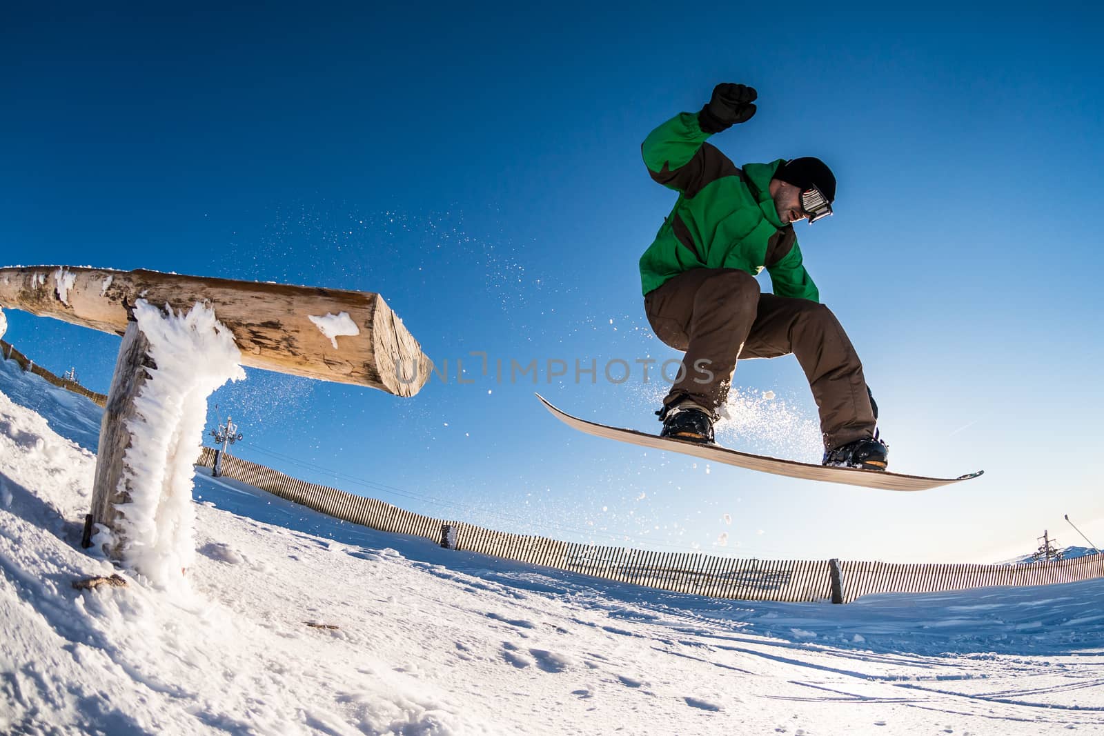 Snowboarder jumping from a wood rail against blue sky.