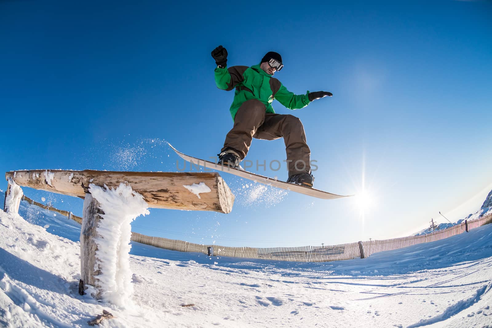 Snowboarder jumping from a wood rail against blue sky.