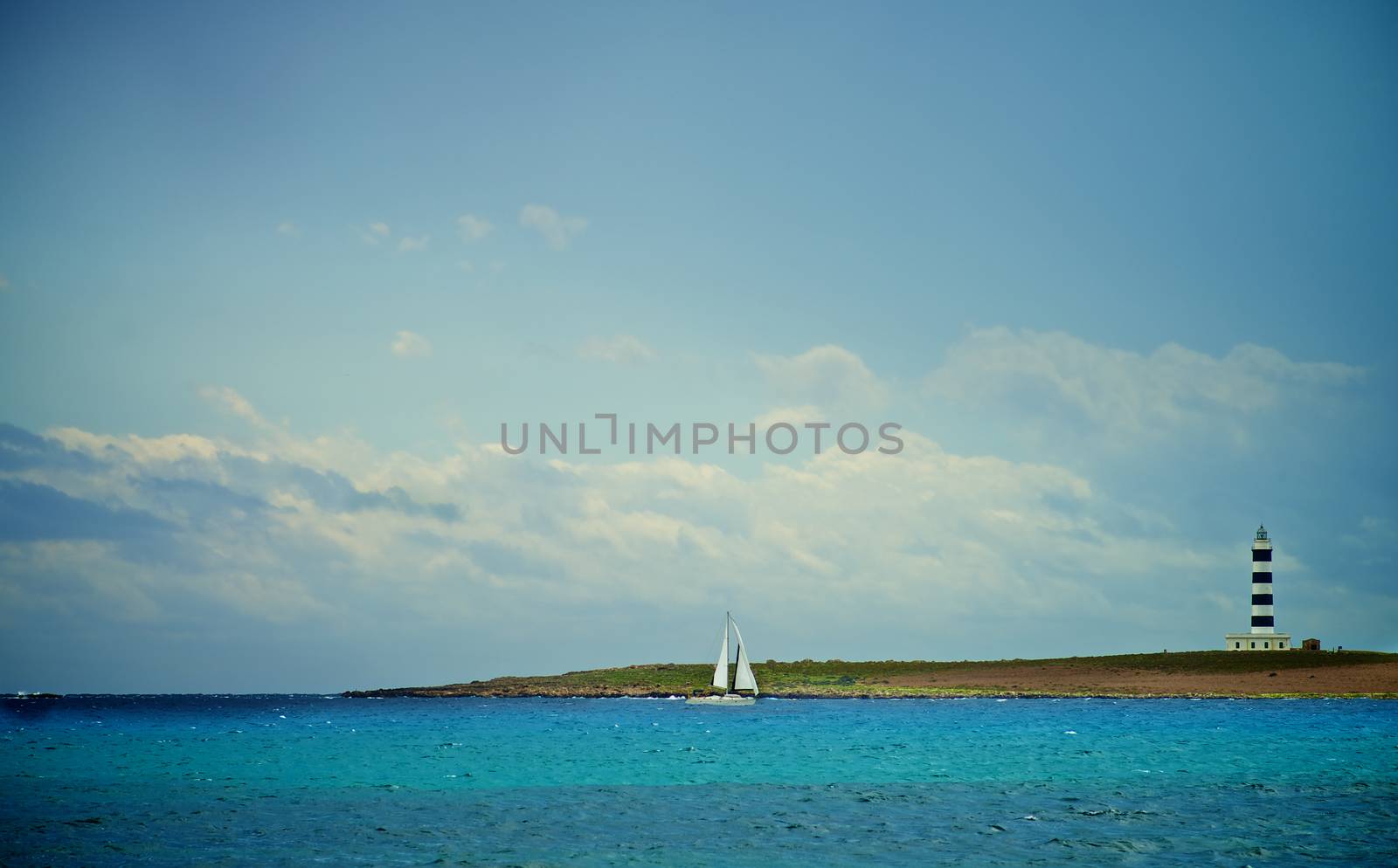 Idyllic Summer Seascape with Small Sailboat and Lighthouse near South Coast of Menorca, Balearic Islands