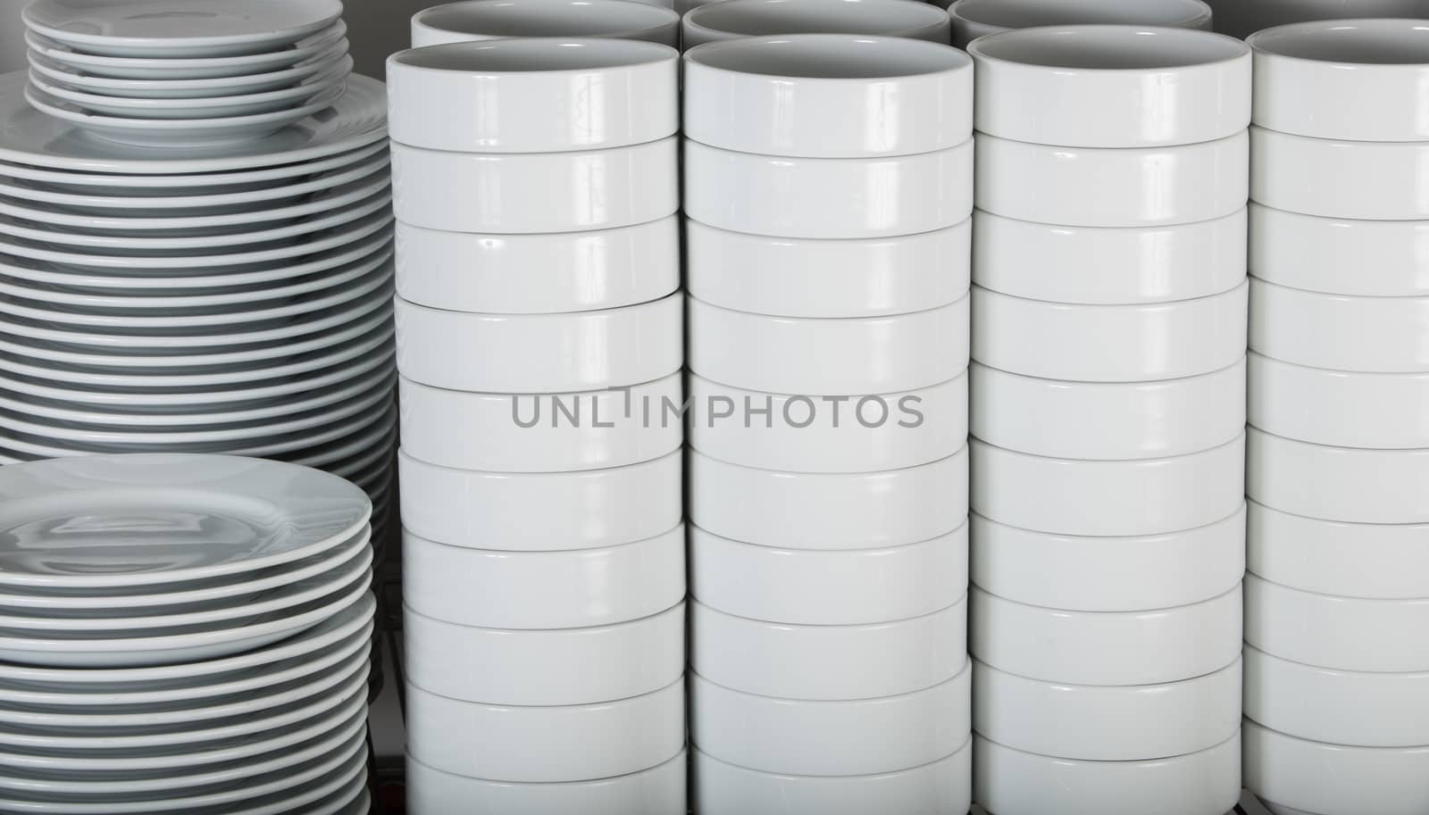 stacks of many white plates on a wire rack shelf in a commercial kitchen
