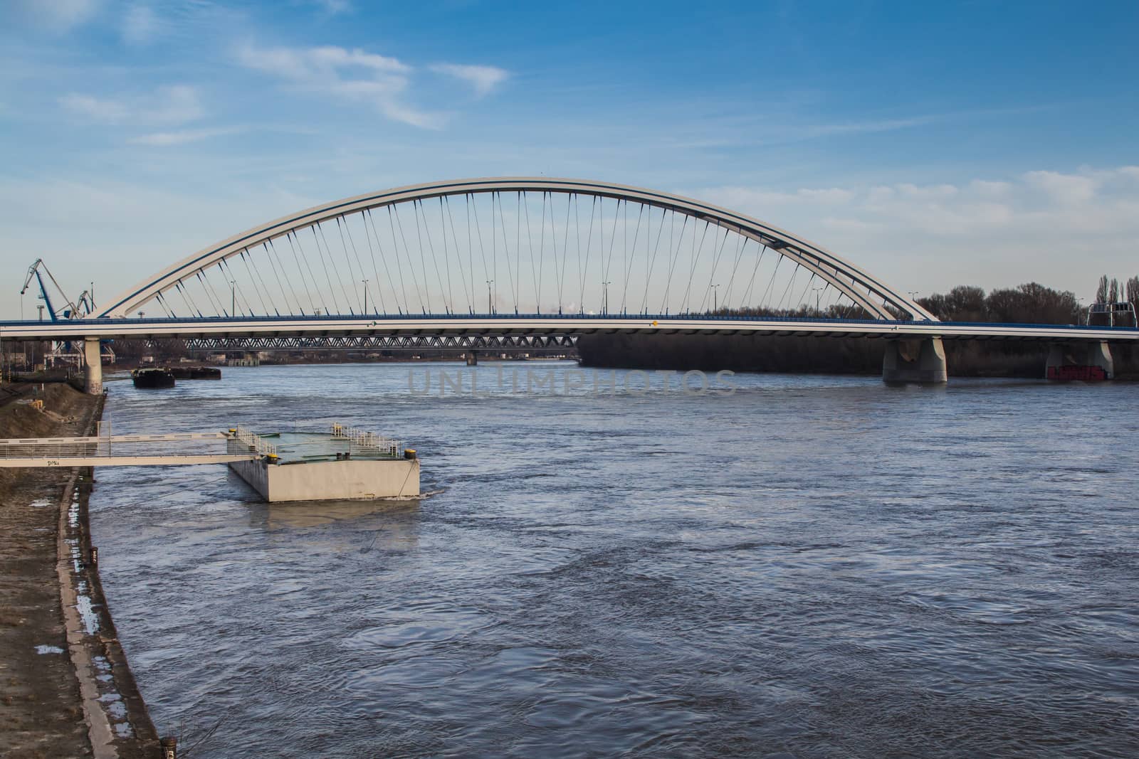 Arch of the bridge across river Danube. Wild water of the river. Blue sky with some white clouds.