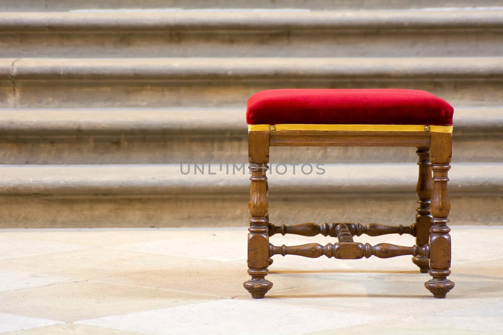 Old wooden stool with red seat and the stairs in the background.