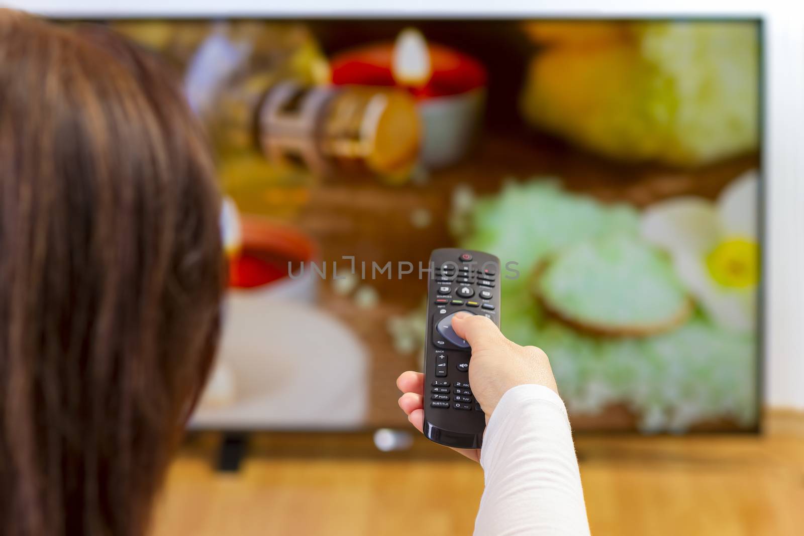 Young woman sitting on sofa holding tv remote and surfing progra by manaemedia