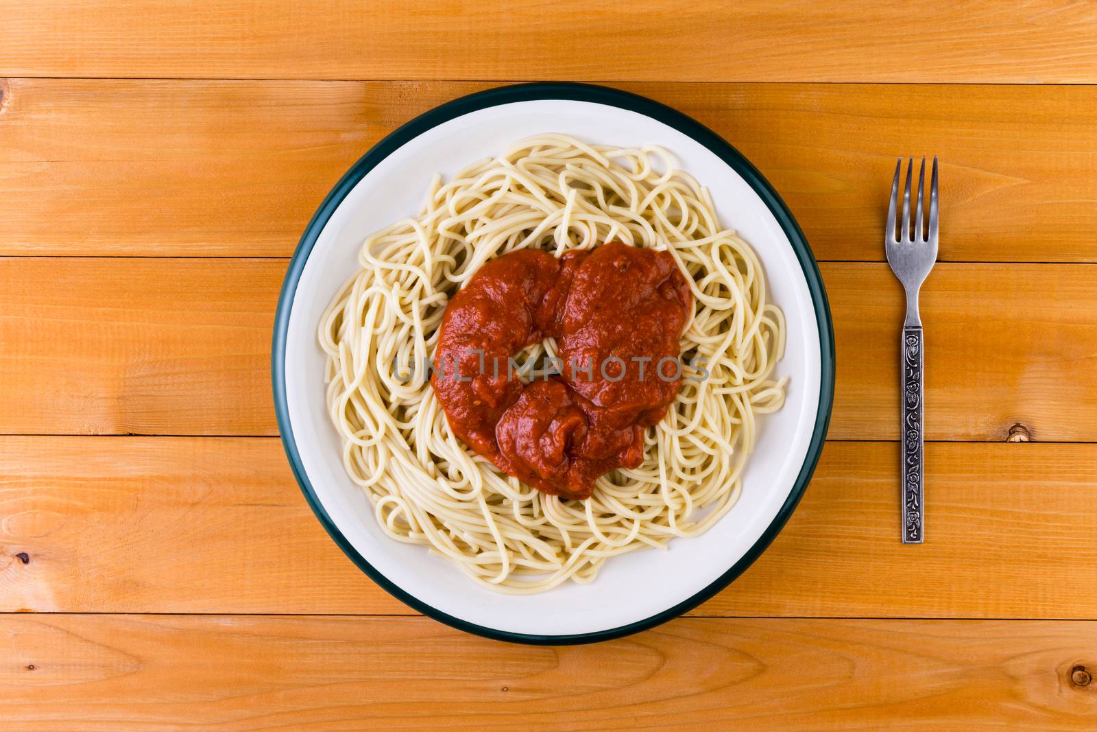 Overhead view of a plate of Italian spaghetti pasta served with a savory tomato sauce on a wooden garden table for a tasty lunch