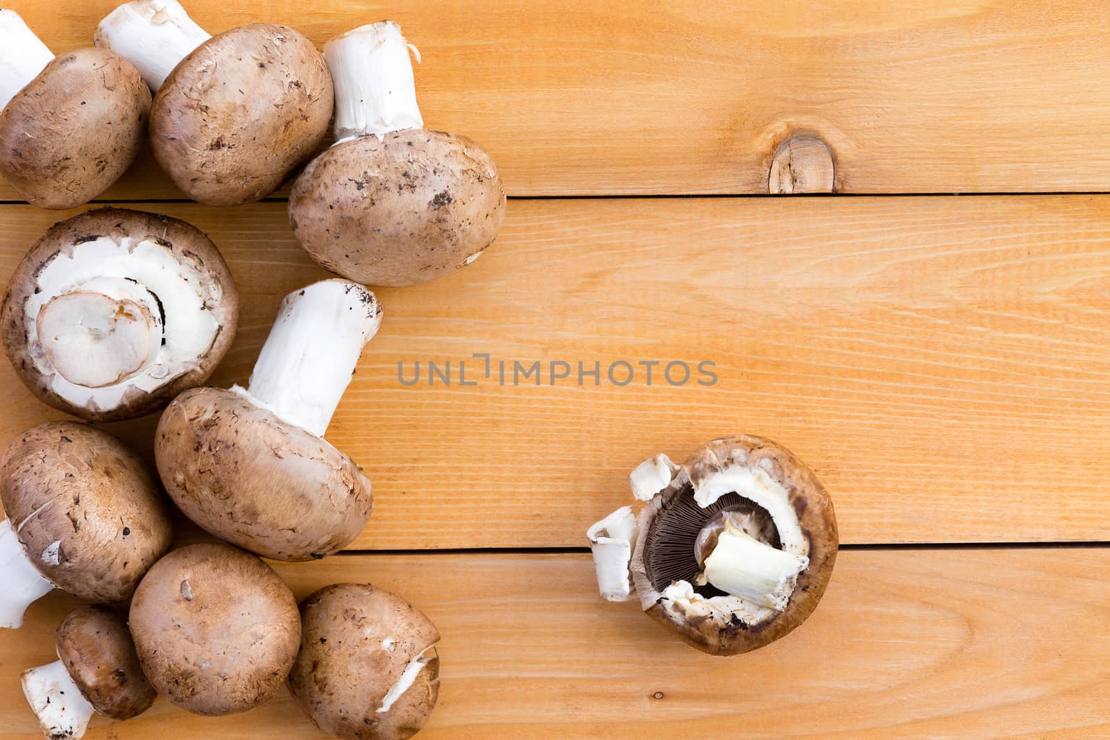 Fresh organic baby bella mushrooms for use as a savory ingredient in cooking and salads on a wooden kitchen table, viewed from above