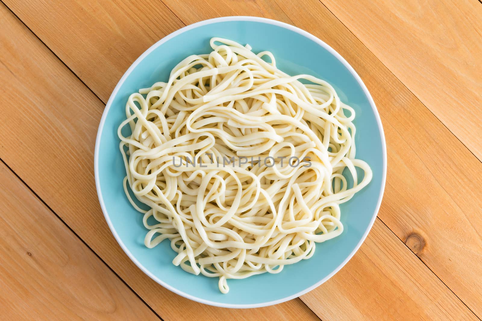 Plated of freshly boiled plain spaghetti served on a blue plate on a wooden garden table with diagonal planks, overhead view