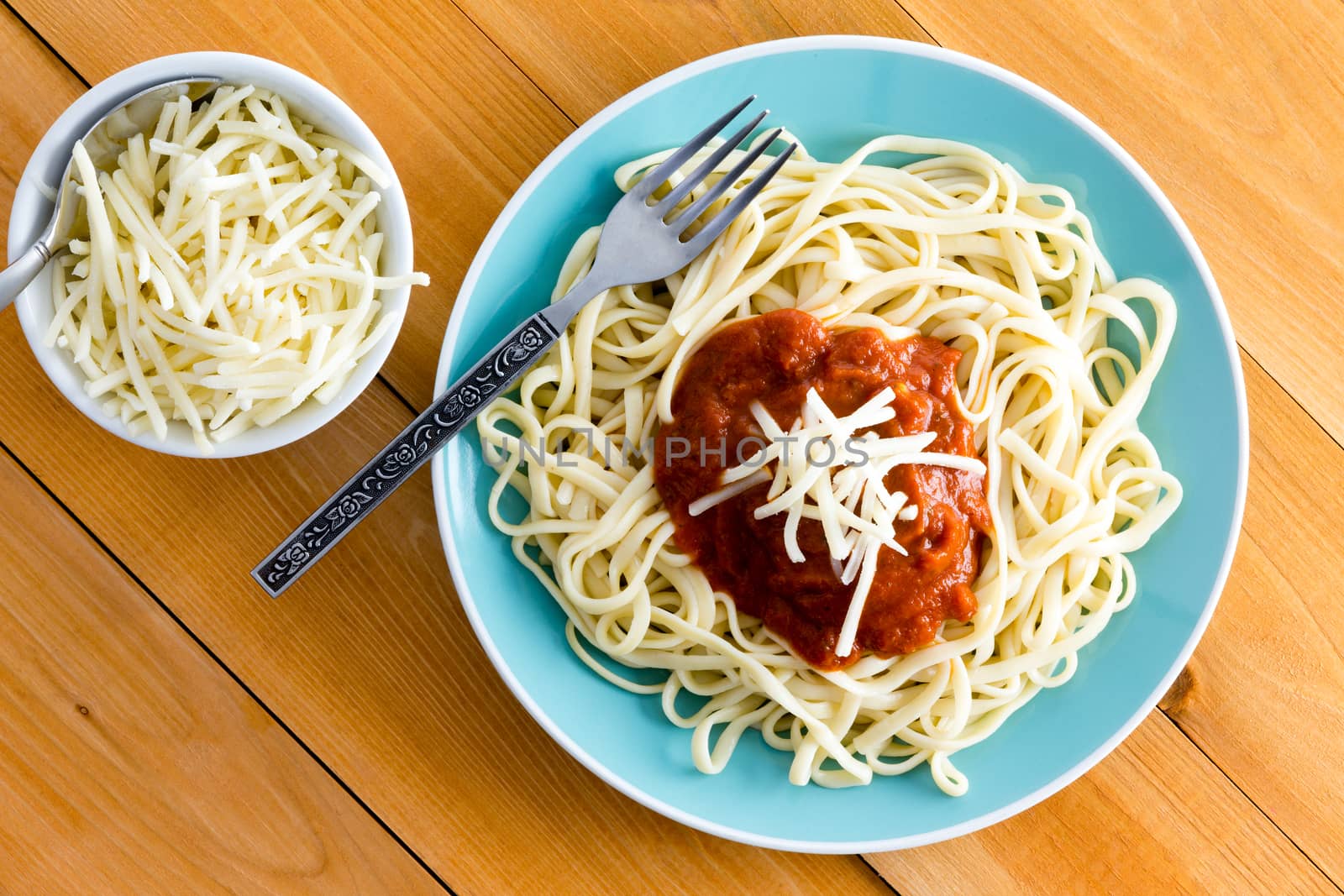 Italian spaghetti Bolognese garnished with grated gruyere cheese with a side dish containing additional cheese alongside, overhead view on a wooden table